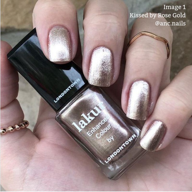 A hand wearing metallic rose gold nail polish holds a bottle of "Kissed by Rose Gold" by LONDONTOWN. The cruelty-free and vegan formula ensures stunning nails with a conscience. Text in the upper right corner reads "Image 1 Kissed by Rose Gold @anc.nails.