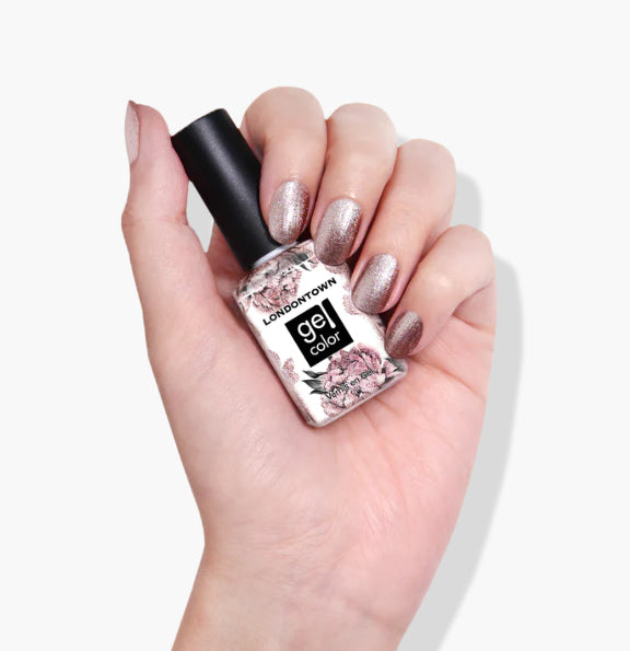 Hand with glittery nail polish holds a bottle labeled "Kissed by Rose Gold" from LONDONTOWN, featuring a floral design.