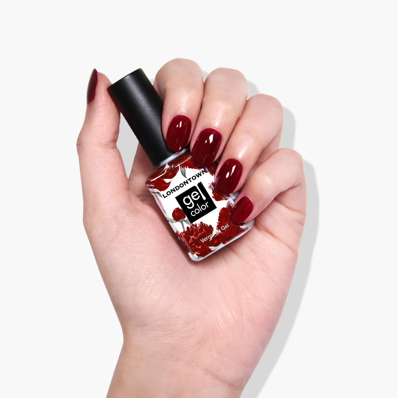 A hand with maroon-colored gel nail polish holds a bottle of Lady Luck by LONDONTOWN vegan gel color nail polish.