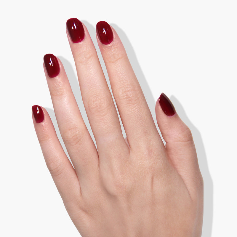 A hand with fingers spread, showing manicured nails painted in a gradient of dark to light red vegan gel color from LONDONTOWN's Lady Luck collection.