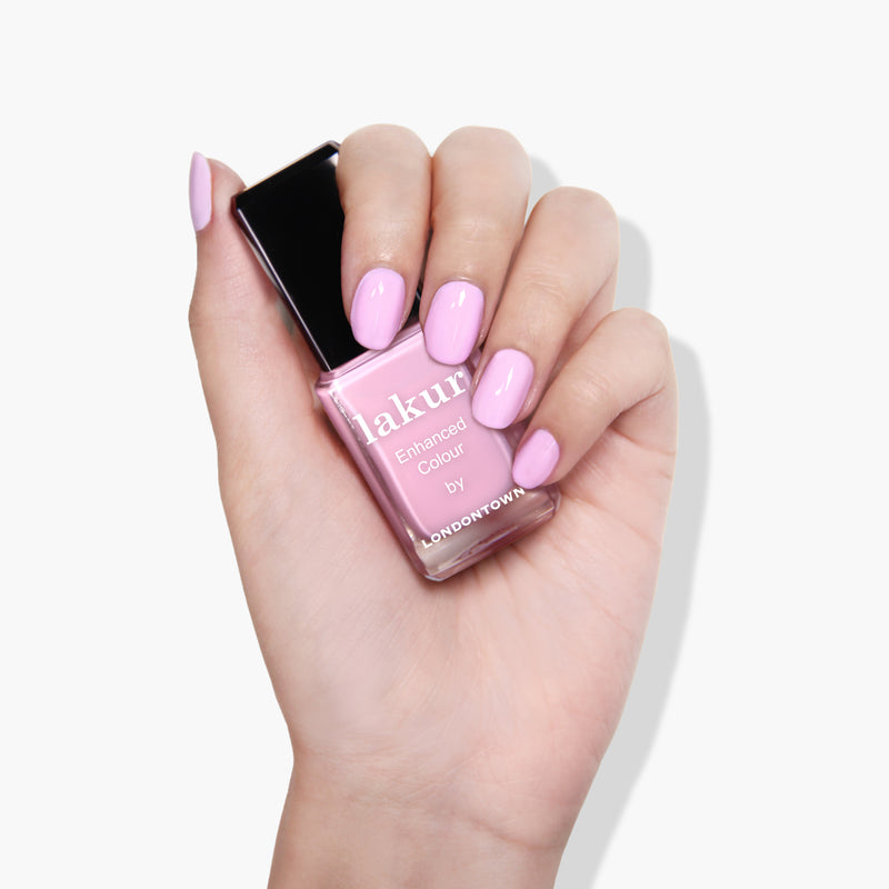 A hand with manicured nails painted in muted pink holding a bottle of pink nail polish labeled "Lemonade Pop by LONDONTOWN," a vegan, cruelty-free product.