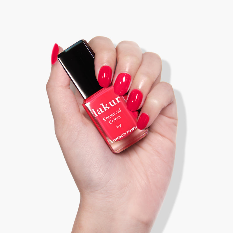 A hand with red-painted nails holds a bottle of pink nail polish labeled "London Calling" by LONDONTOWN, set against a white background. This vegan, cruelty-free nail polish is perfect for ethical beauty enthusiasts.