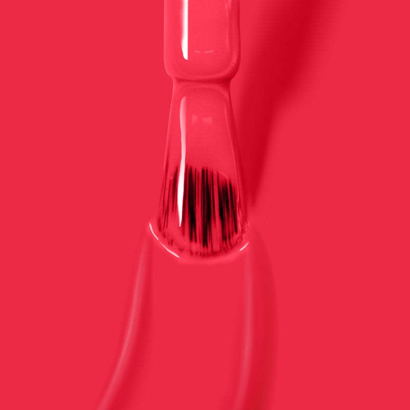 Close-up of a nail polish brush dipped in London Calling, LONDONTOWN's bright red, vegan cruelty-free nail polish, with the bristles coated in the vibrant color.