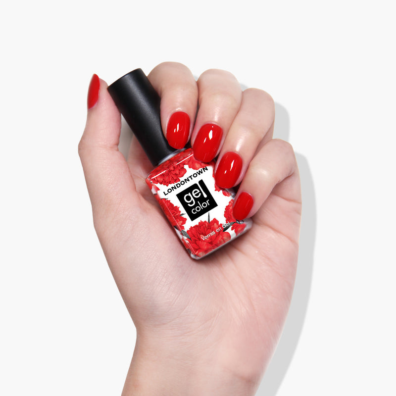 A hand with manicured red nails holds a bottle of LONDONTOWN's Londoner Love Gel Color nail polish, ready to shine under UV/LED light.
