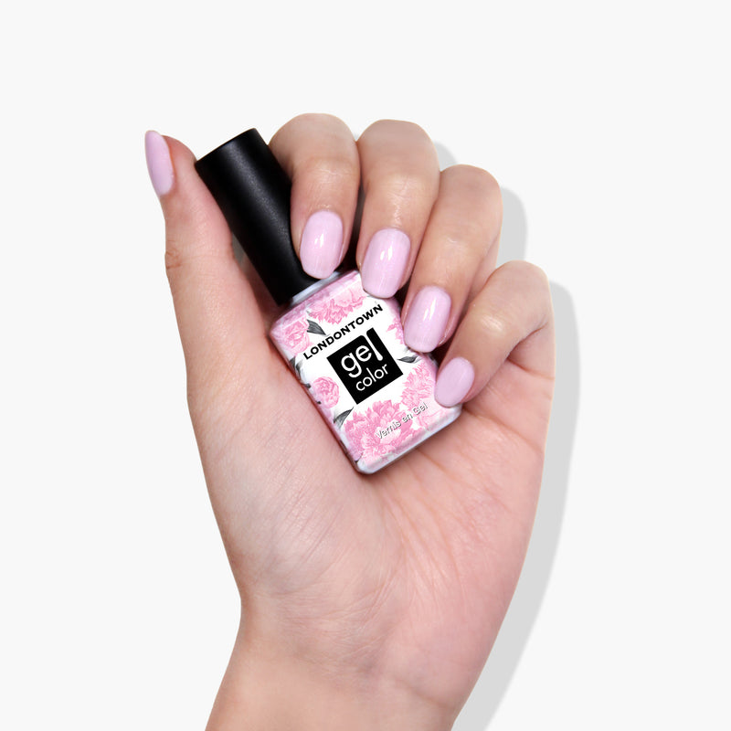A hand with light pink polished nails holding a bottle of LONDONTOWN's "Love Bug" vegan gel color nail polish, featuring a floral label and promising extended wear.