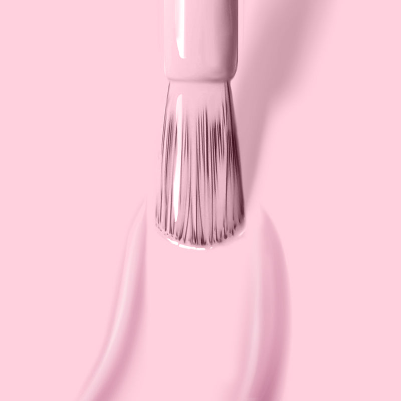 Close-up of a LONDONTOWN nail polish brush applying the vegan gel color "Love Bug" in a light pink crème shade on a pink surface, promising extended wear.