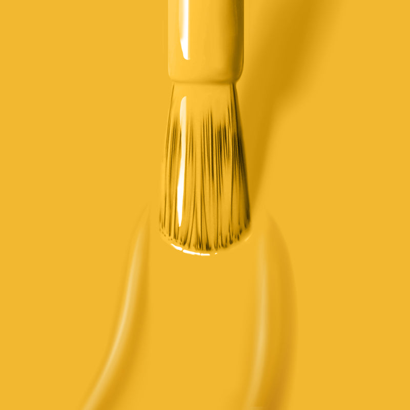 A close-up of a paintbrush tip applying LONDONTOWN's Mango vegan, cruelty-free yellow paint on a matching yellow background.