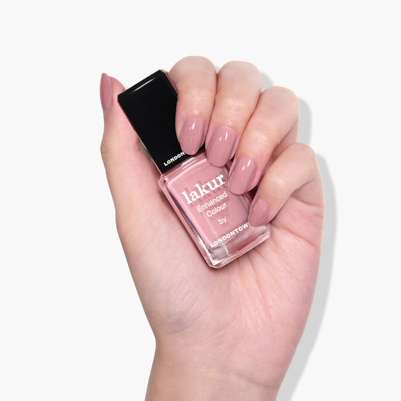 A hand holding a bottle of LONDONTOWN's Lakur Enhanced Colour vegan, cruelty-free nail polish in the shade "Mauve Over," with nails painted in a matching color.
