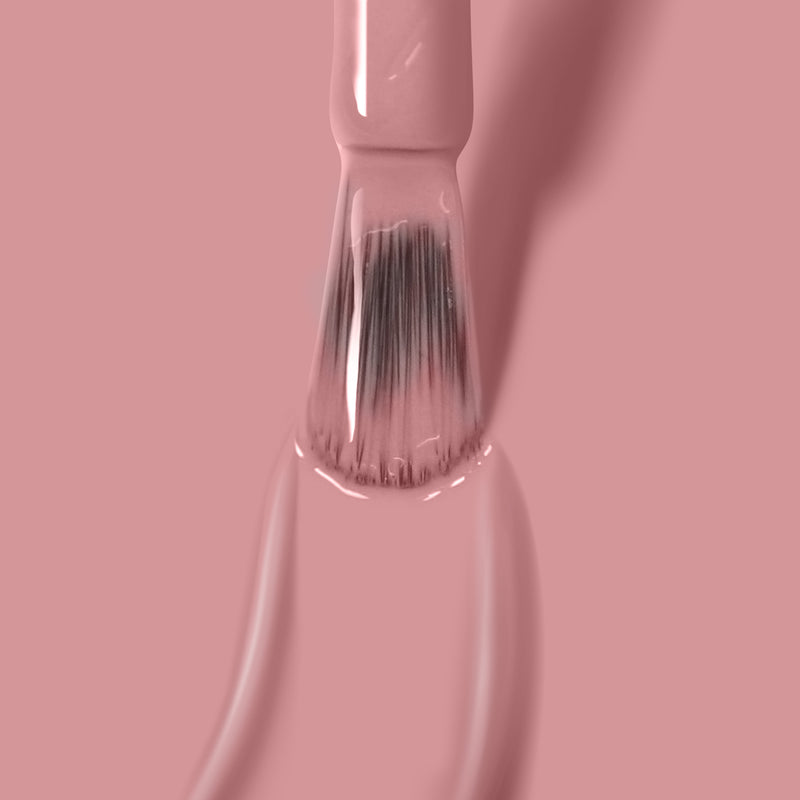 Close-up of a brush applying LONDONTOWN's Mauve Over gel nail polish, with bristles coated in the streak-free color against a pink background.