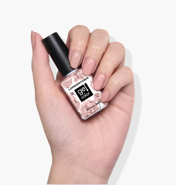 A hand with manicured nails holds a bottle of LONDONTOWN Mauve Over gel color nail polish against a white background, showcasing its streak-free color.