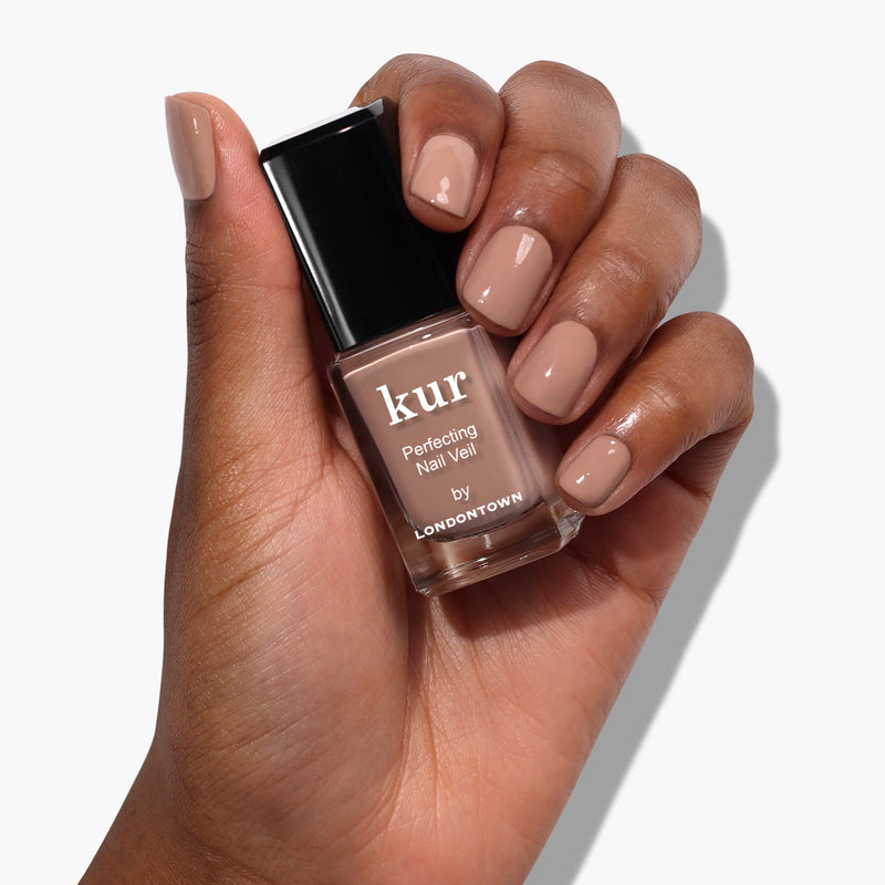 A hand with manicured nails holds a power-packed bottle of Perfecting Nail Veil #6 from LONDONTOWN, offering a hint of color and care.
