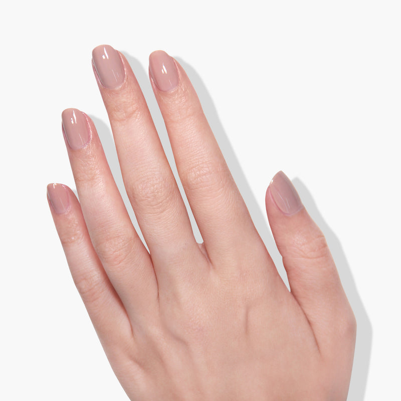 Close-up of a light-skinned hand with a manicure. The nails are short and painted with LONDONTOWN's Milk Tea, a glossy, deep nude crème polish, cured under UV/LED light for that perfect shine.