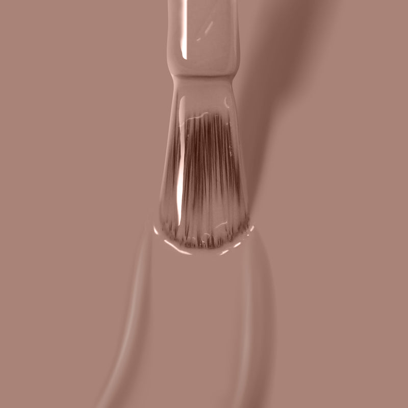 Close-up of a LONDONTOWN Milk Tea vegan cruelty-free nail polish brush applying deep nude crème polish on a matching beige background.