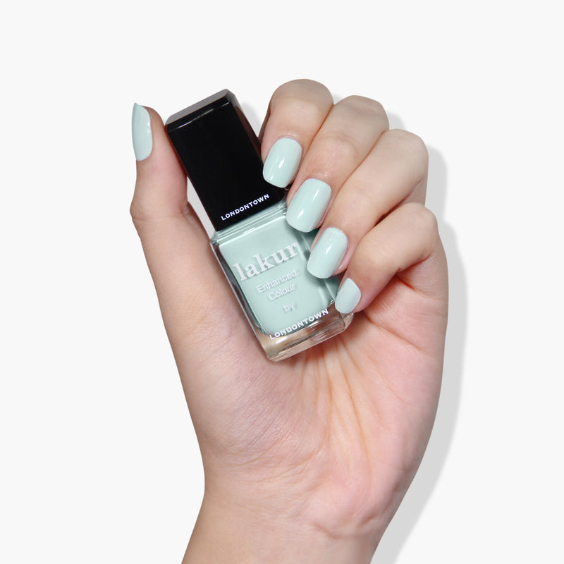 A hand holding a bottle of LONDONTOWN's Mint No Chip, a cruelty-free and vegan nail polish, in a light mint green shade.