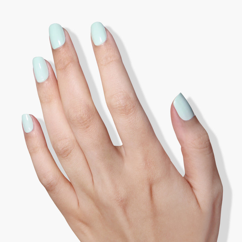 A hand with light skin tone and short fingernails painted in LONDONTOWN's Mint No Chip, a pale mint creme green color, on a white background, showcasing a cruelty-free, vegan nail polish.