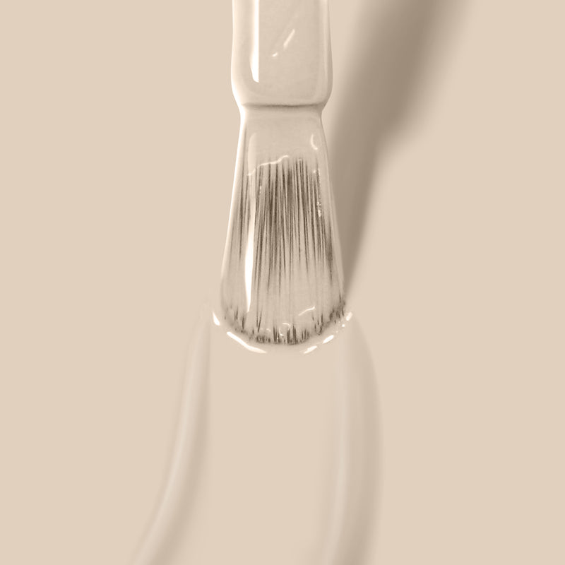 Close-up of a Murray Me paintbrush from LONDONTOWN, dipped in beige French vanilla cream-colored paint on a matching background.