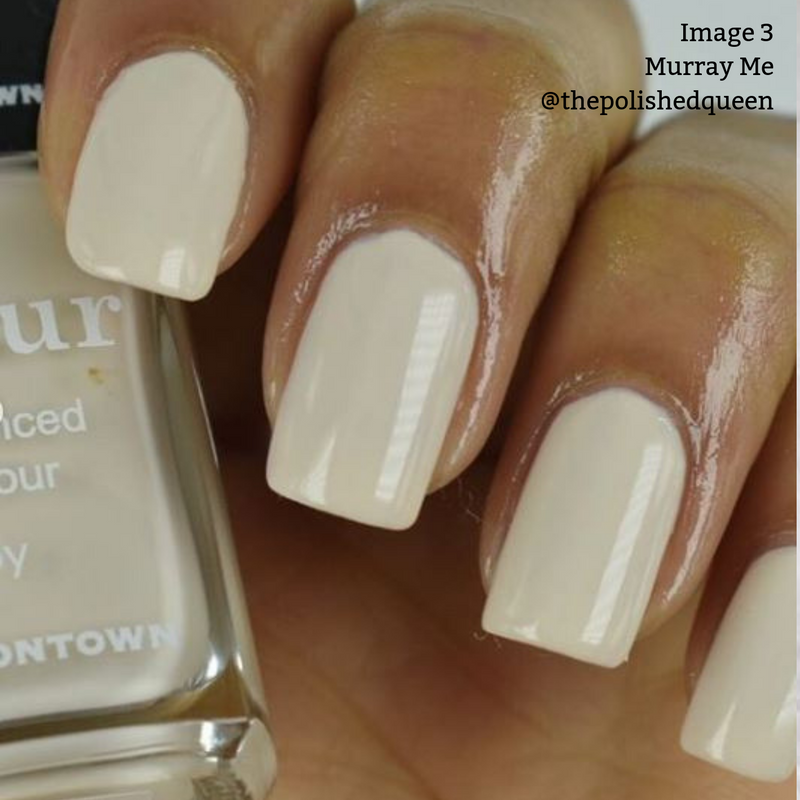 Close-up of a hand with light beige polished nails, holding a bottle of vegan, cruelty-free nail polish labeled "Murray Me'' by LONDONTOWN. The French vanilla cream hue adds an elegant touch.