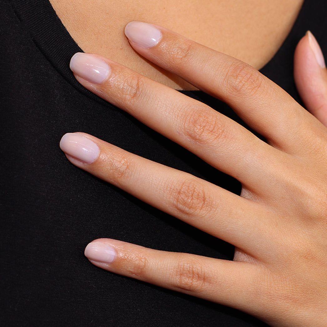 A hand with neatly manicured nails, enhanced to perfection with LONDONTOWN's Illuminating Nail Concealer (Professional) in a nude shade, rests on a black fabric surface.
