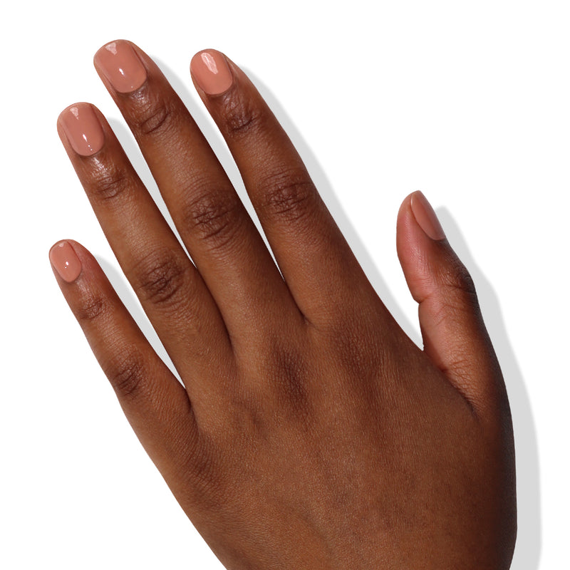 A left hand with medium brown skin tone displays a manicured set of short, shiny light beige nails against a white background, showcasing the power-packed care taken to achieve the perfect color using Perfecting Nail Veil #5 by LONDONTOWN.