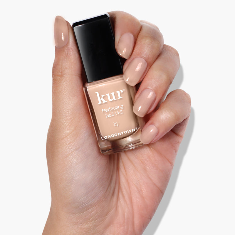 A hand holding a bottle of nude-colored nail polish labeled "Perfecting Nail Veil #1 by LONDONTOWN." The nails, painted with the same care, reflect the power-packed color.