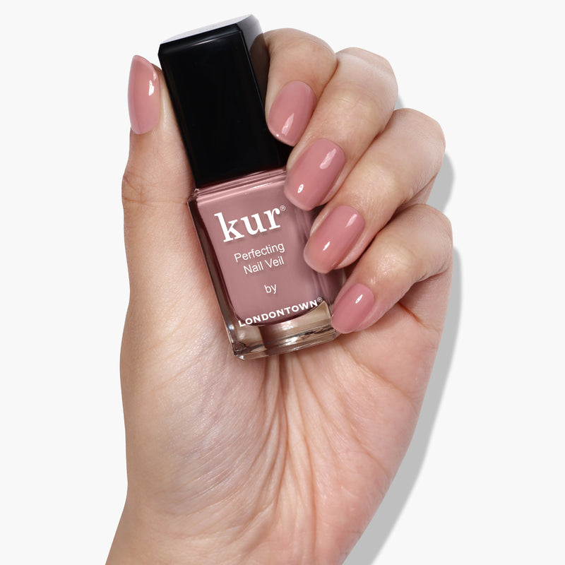 A hand holding a bottle of LONDONTOWN's Perfecting Nail Veil #3, displaying manicured nails painted in a similar shade as the power-packed nail polish.