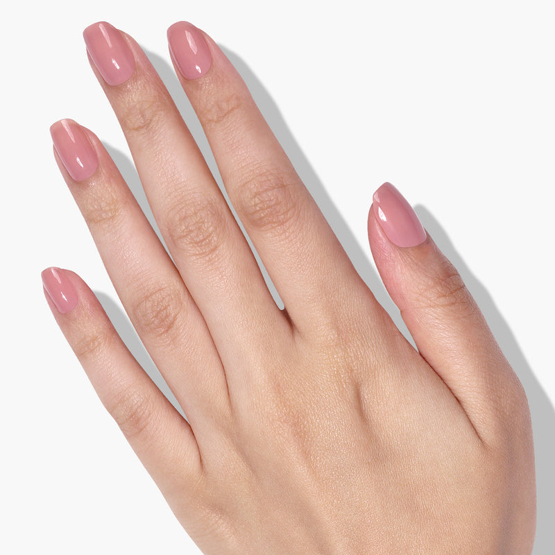 A hand with manicured nails painted in LONDONTOWN's Perfecting Nail Veil #3, a light pink shade, against a white background, radiating subtle color and showing meticulous care.