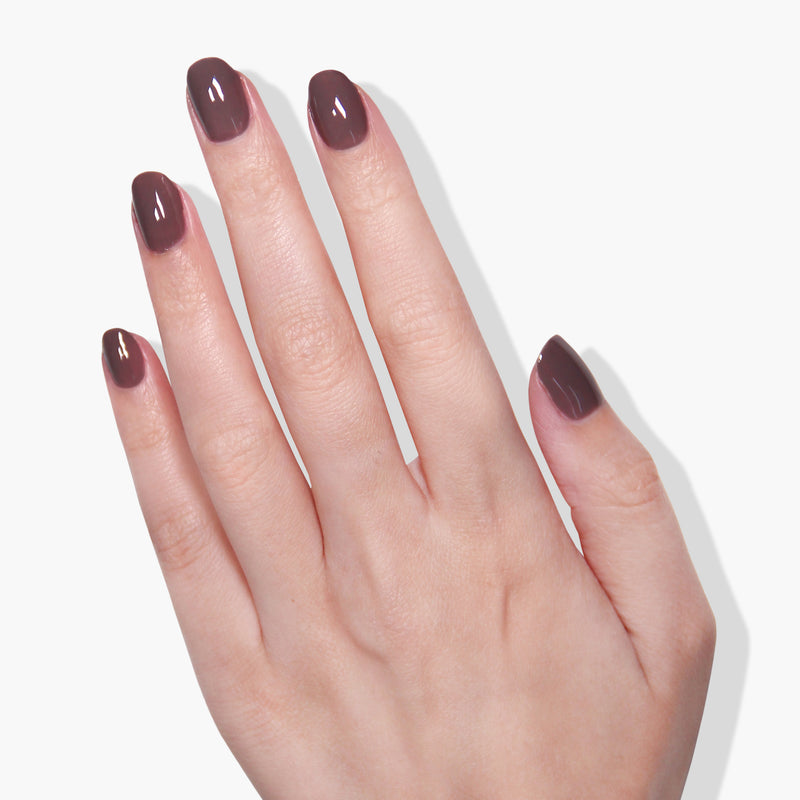 A hand with neatly manicured nails painted in LONDONTOWN's Natural Charm, a creamy mauve purple shade, displayed against a white background.
