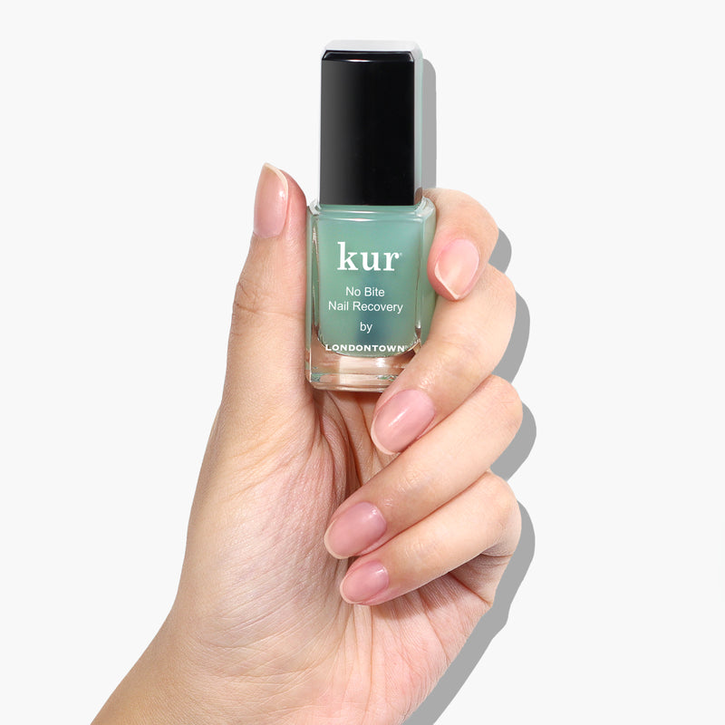 A hand holding a small bottle of LONDONTOWN's No Bite Nail Recovery polish against a white background, promoting better habits for healthy-looking nails.