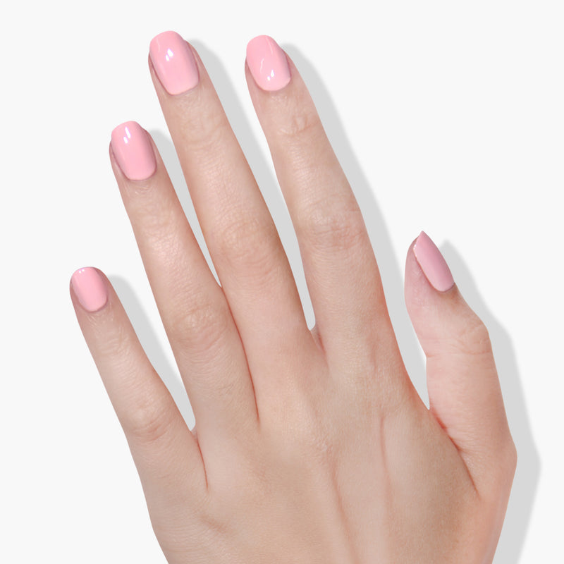 A close-up image of a hand with neatly manicured nails painted in LONDONTOWN's pastel pink "Out of Office" nail polish, enhanced by the Florium Complex, against a white background.