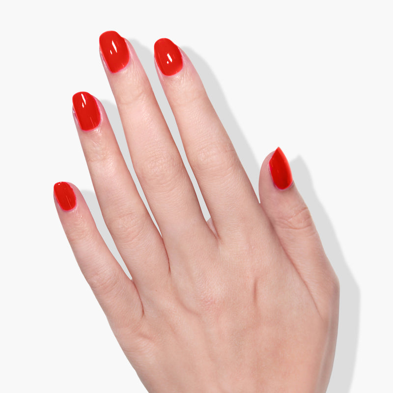 A hand with neatly manicured nails painted in LONDONTOWN's Piccadilly Square, an ultra-bright blood orange crème polish, against a white background.
