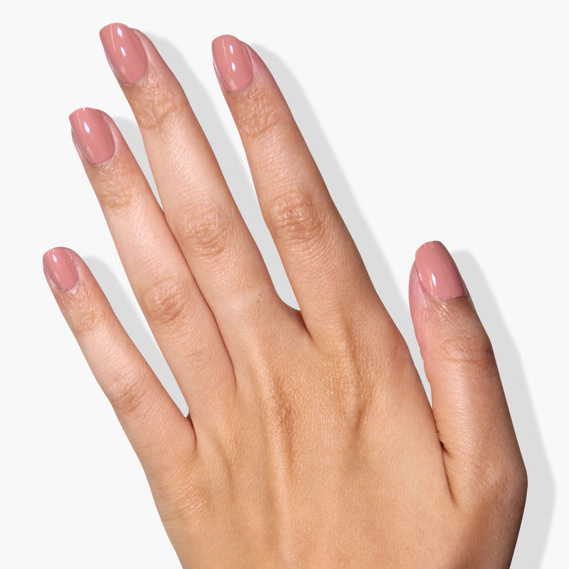 A hand with manicured nails painted in a light pink Pink Sands Nail Polish by LONDONTOWN, infused with the Florium Complex, against a white background.