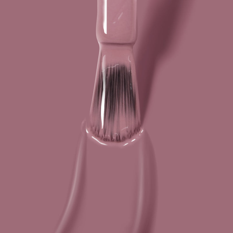 A brush applies a coat of LONDONTOWN's Plush, a smooth, mauve crème nail polish, on a surface.