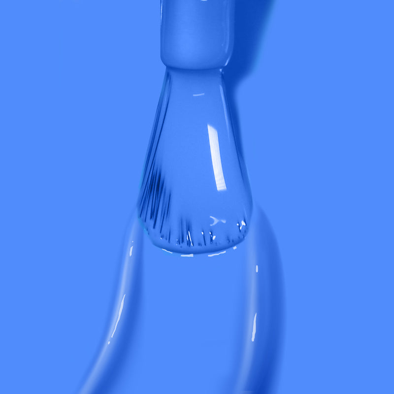 Close-up of a paintbrush applying LONDONTOWN's Poolside Dreams nail polish in medium azure evenly on a smooth surface, with a light reflection visible on the brush bristles.