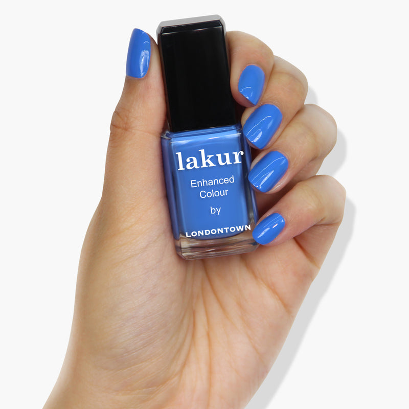 A hand holding a bottle of vegan, cruelty-free nail polish labeled "Poolside Dreams by LONDONTOWN" with nails painted in the same bright blue color.
