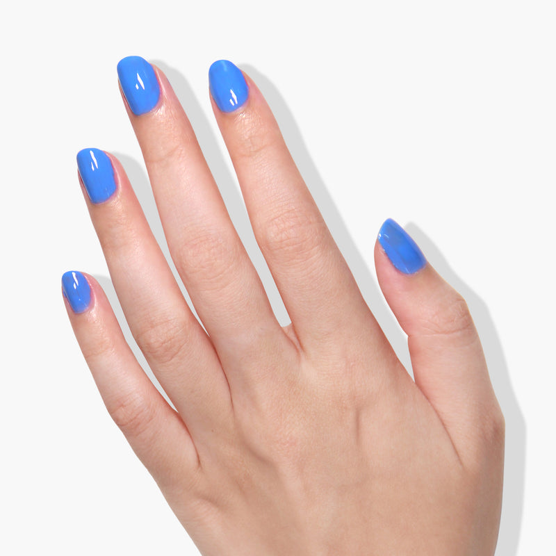 A hand with short, rounded fingernails painted in Poolside Dreams by LONDONTOWN, a glossy darling blue color perfect for catching the light of any UV/LED lamp, set against a white background.
