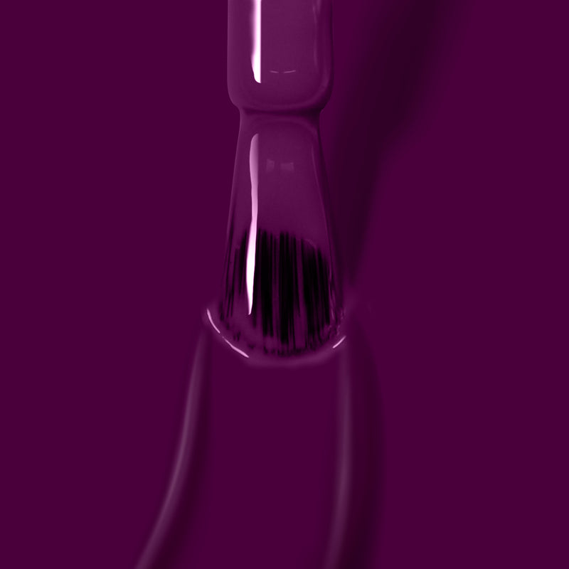 Close-up of a vegan cruelty-free nail polish brush dipped in deep warm plum crème from the Portobello Plum nail polish by LONDONTOWN, with polish coating the bristles and dripping slightly.