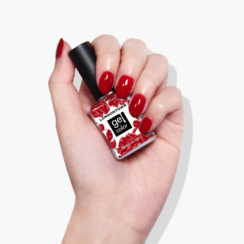 Hand with red polished nails holding a bottle of LONDONTOWN’s Ring Me gel color nail polish, perfect for curing under UV/LED light.