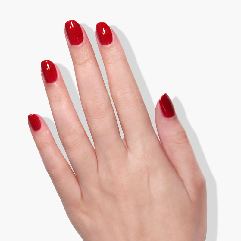 A hand with neatly manicured nails painted in glossy Ring Me red crème from LONDONTOWN gel color, against a white background.
