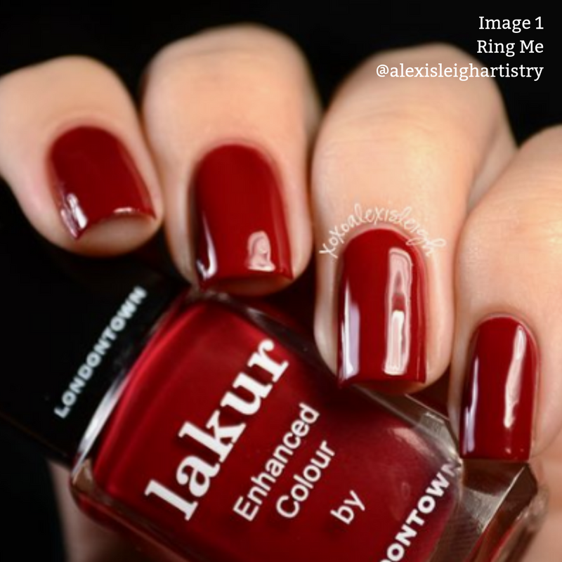 Close-up of a hand with neatly manicured nails painted in deep red vegan, cruelty-free polish. A bottle of "Ring Me" by LONDONTOWN Red crème nail polish is held between the thumb and index finger, showcasing its PETA certified credentials.