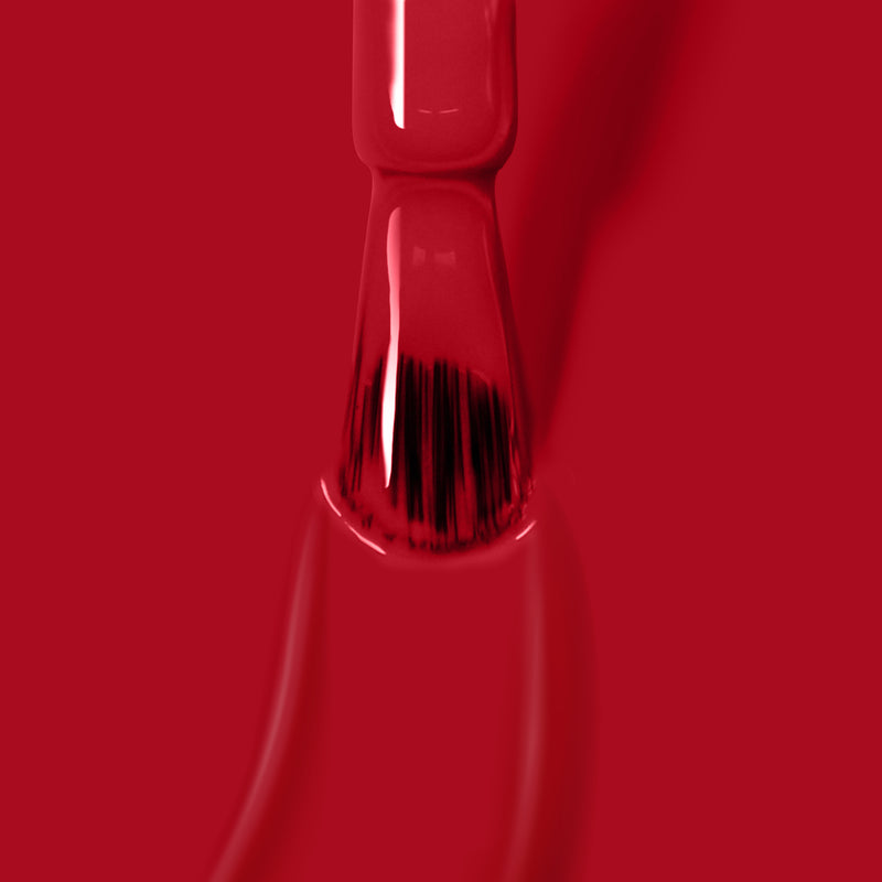 Close-up of a brush applying LONDONTOWN's Ring Me bright red crème nail polish on a surface, with the polish visibly thick around the bristles, seamlessly preparing for its curing under UV/LED light.