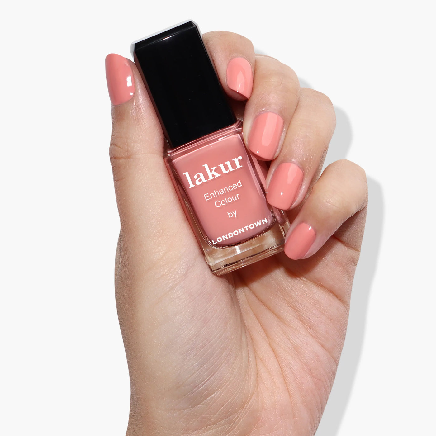 A hand holding a bottle of LONDONTOWN's Rose-Tinted Glasses (Professional) nail polish in a delightful shade of pink, reminiscent of Himalayan pink sea salt, with matching hues applied on the fingernails — perfect for a fresh spring look.