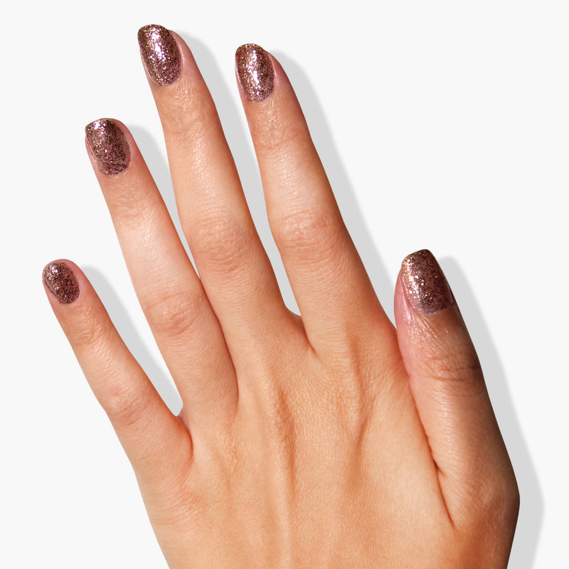 A hand with five fingers showcasing a metallic bronze glitter nail polish on each nail, set against a plain white background—an exquisite example of LONDONTOWN's "Rosé All Day" polish, known for its vegan cruelty-free formula.