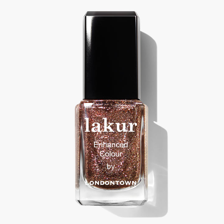 A bottle of LONDONTOWN nail polish in the shade "Rosé All Day," a glittery rose gold hue, with "Enhanced Colour" written on the front. This vegan, cruelty-free gem features a black cap and is part of the sought-after LONDONTOWN polishes collection.