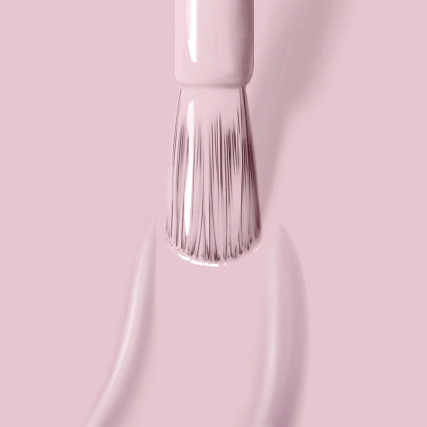 Close-up of a brush applying LONDONTOWN's Rosewater (Professional) light pink, vegan nail polish, leaving smooth, shiny strokes on a pink surface.