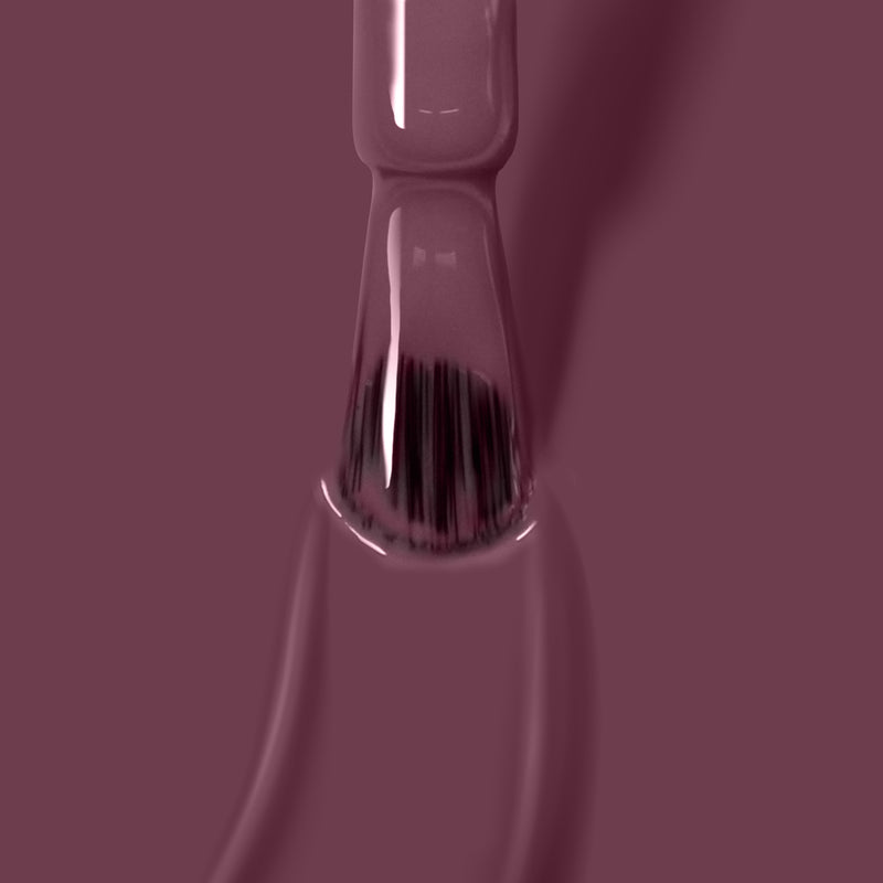 A brush with bristles is coated in glossy, dark mauve liquid, possibly Save the Queen vegan, cruelty-free nail polish by LONDONTOWN, against a solid dark mauve background.
