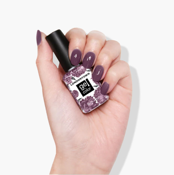 A hand holding a bottle of LONDONTOWN Save the Queen UV/LED Gel Color nail polish with matching purple, cruelty-free nails.