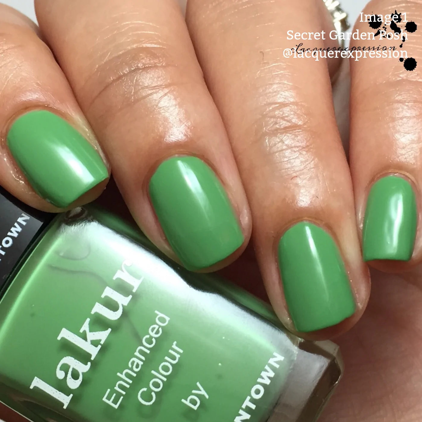 Close-up of a hand with short nails painted in a creamy grassy green nail polish. The bottle, labeled "Secret Garden Posh (Professional)" by LONDONTOWN, is partially visible and held in the same hand, showcasing its vegan cruelty-free formula.