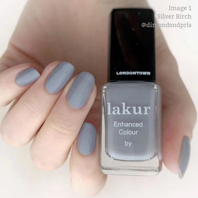 Close-up of a hand with manicured nails painted in light gray, holding a bottle of LONDONTOWN's Silver Birch (Professional) nail polish. This vegan, cruelty-free nail polish offers a chic look without compromising on ethics.