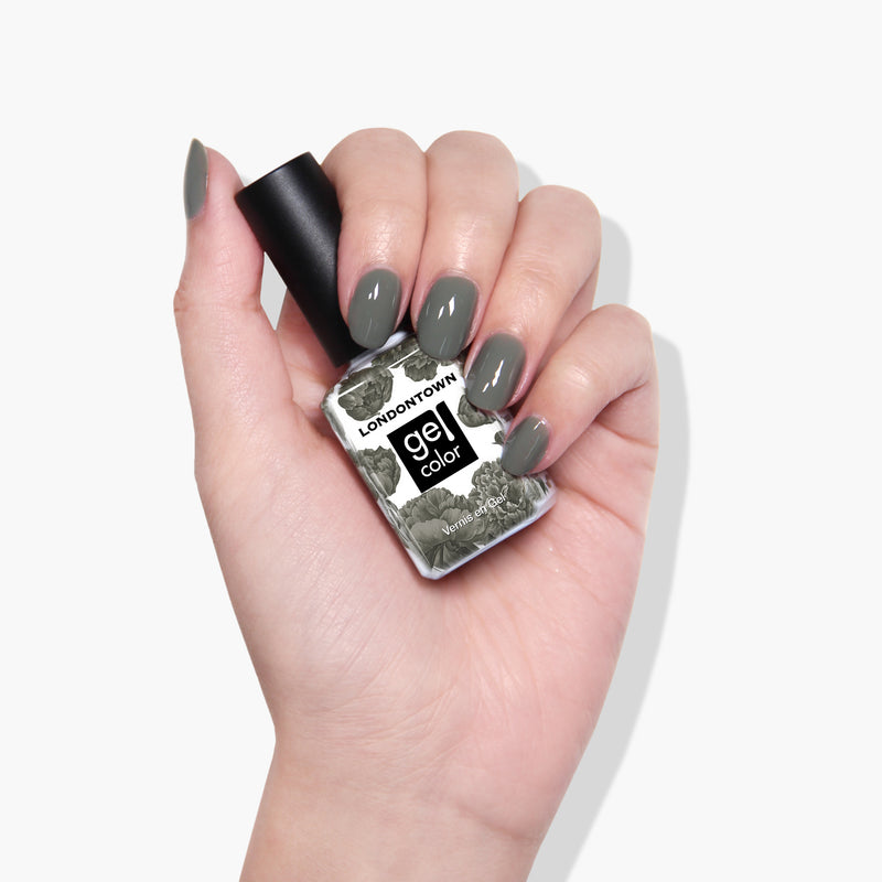Hand holding a bottle of LONDONTOWN Star Moss gel color nail polish with nails painted in a matching olive shade, all in a vegan-friendly formula.