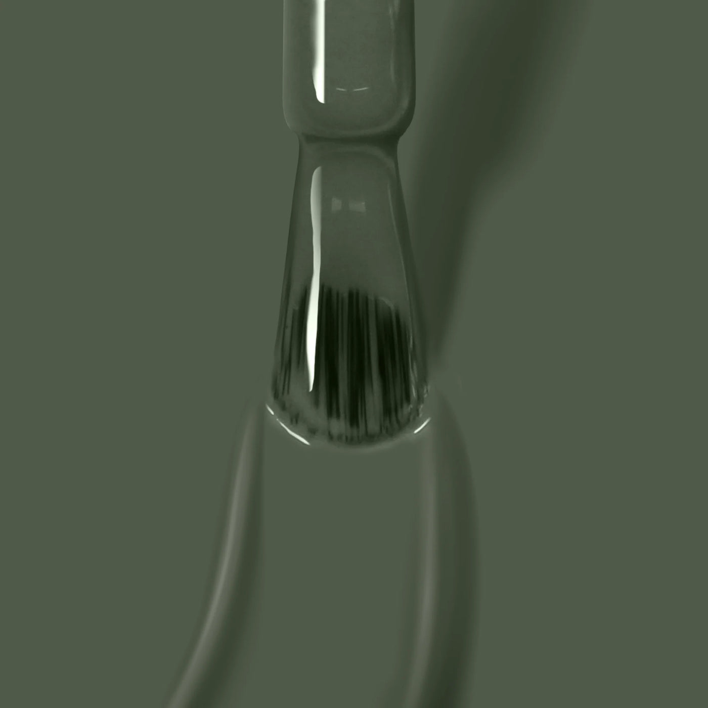 Close-up of a paintbrush dipped in gray liquid paint with bristles immersed and droplets on the handle, featuring the olive shade "Star Moss (Professional)" from LONDONTOWN's cruelty-free, vegan line.
